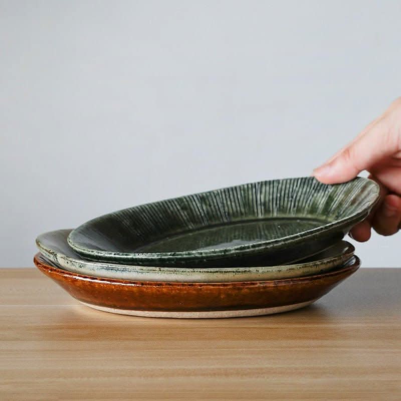 Nishida Muyu oval deep plate stack: forest green, earth brown ceramic sushi dishes on wooden table.